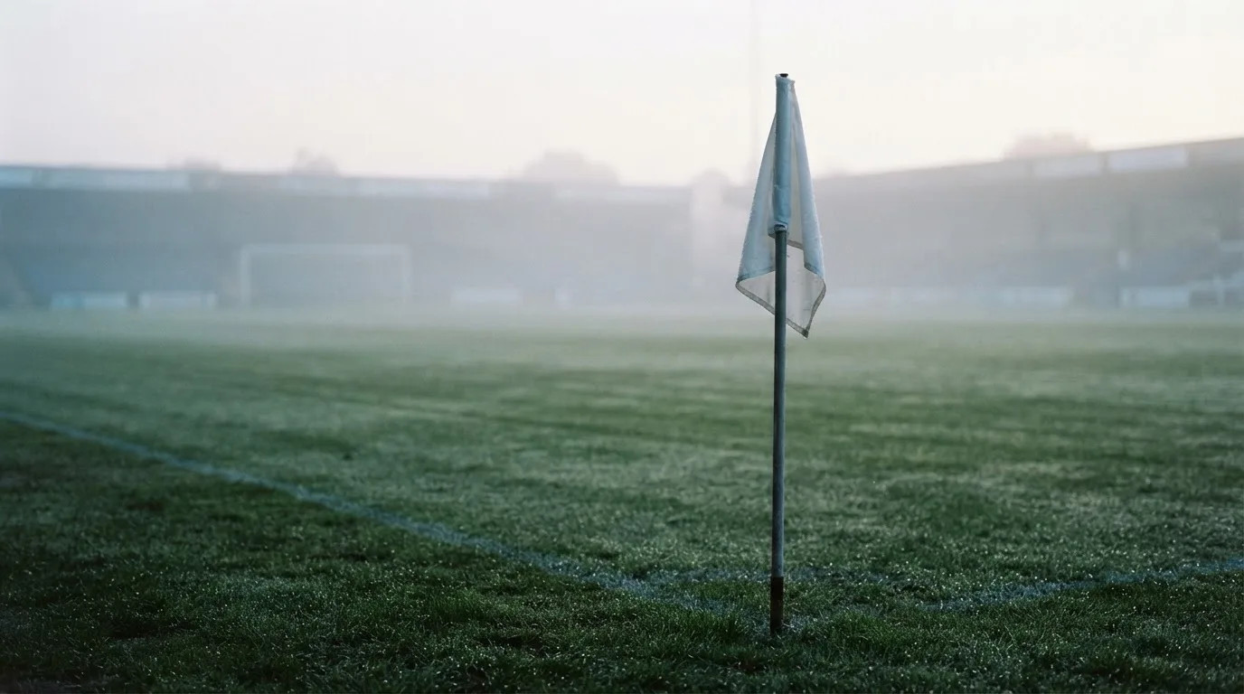Eine Eckfahne steht am Morgen auf nassem Rasen, Tautropfen hängen im Gras und über dem Platz liegt leichter Dunst.