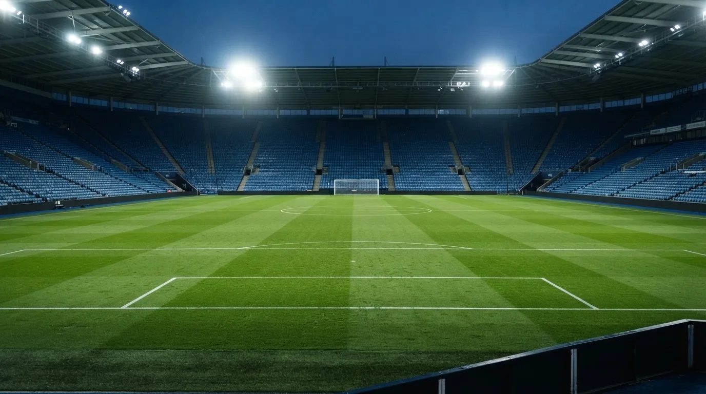 Leere Tribünenränge eines Fussballstadions in der Abenddämmerung, über dem Rasen leuchten die Flutlichter.