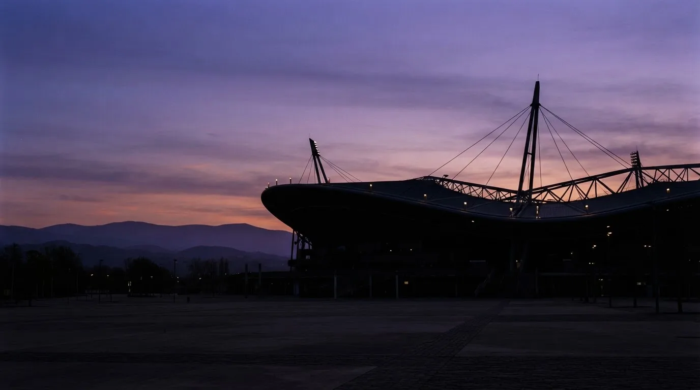Die Silhouette eines Stadiondachs vor dem violetten Abendhimmel, dahinter eine Hügelkette.
