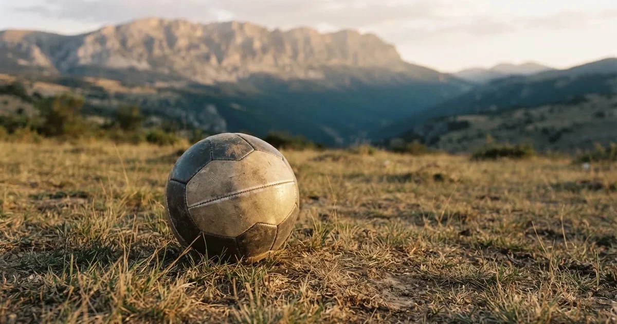 Ein Fussball auf einem staubigen Rasenstück in der Abendsonne, im Hintergrund eine hohe Bergkette