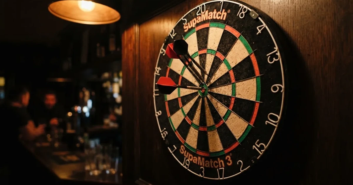 Drei Dartpfeile stecken in einer Dartscheibe an einer Holzwand in einer dämmrigen Kneipe, warmes Lampenlicht fällt von oben
