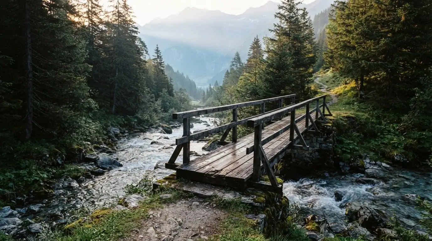 Eine alte Holzbrücke führt über einen Bergbach im Morgenlicht, Tannen säumen das Ufer