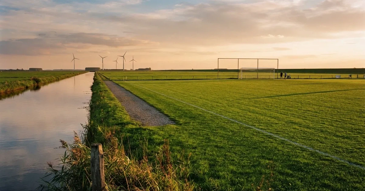 Ein Fussballplatz neben einem Kanal in flachem Land mit Windrädern am Horizont, Abendlicht liegt über dem Rasen