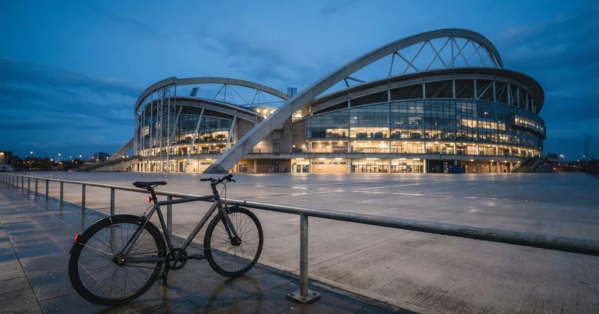 Ein Stadionrund von aussen in der Dämmerung, Betonbögen und leerer Vorplatz, ein Fahrrad lehnt am Geländer.