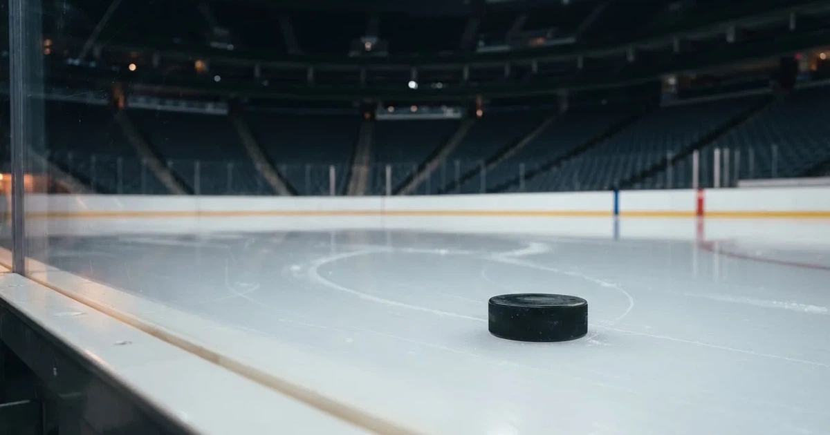 Ein Eishockeypuck liegt auf einer glatten Eisfläche, im Hintergrund erheben sich die dunklen Ränge einer leeren Halle.
