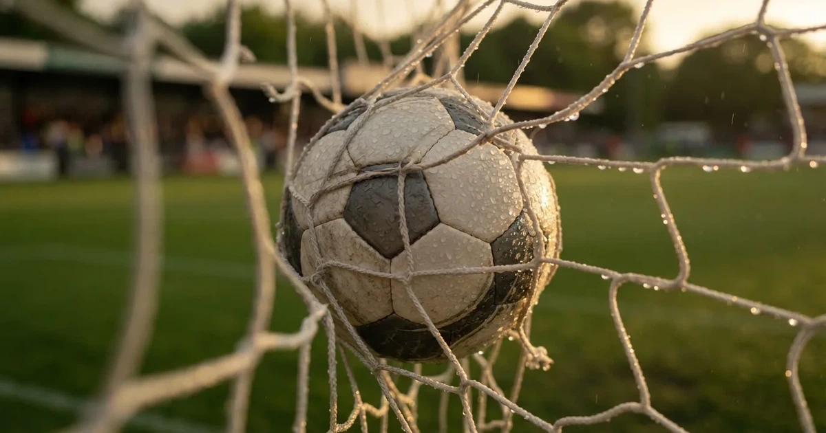 Ein Fussballnetz in Nahaufnahme, in dem ein Ball hängt, Wassertropfen glänzen auf den Maschen.
