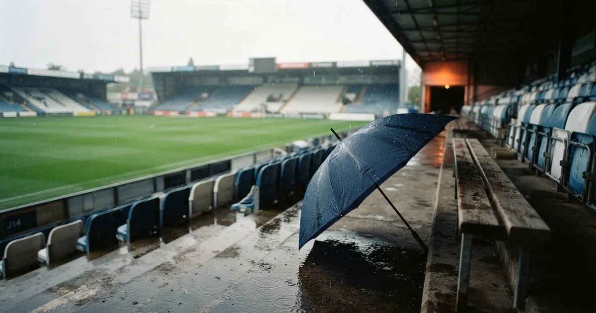 Ein offener Regenschirm lehnt an einer leeren Tribünenbank, Regen fällt auf die Stufen eines Stadions