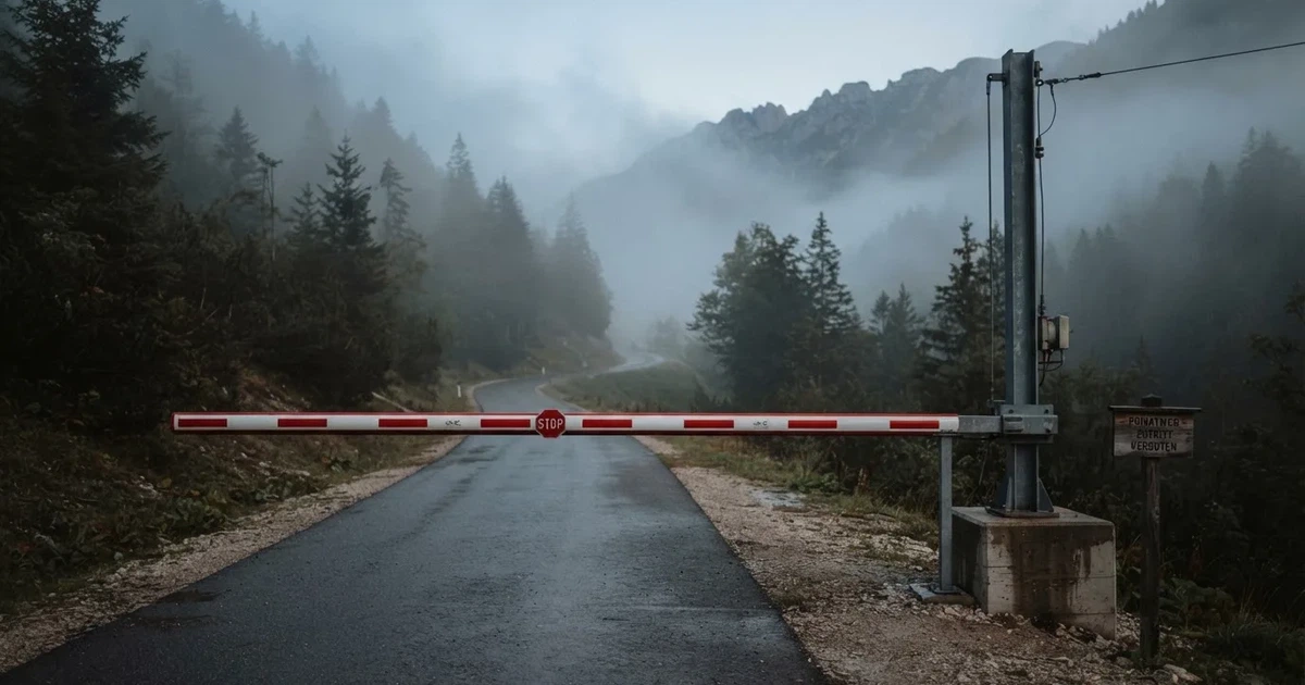 Ein geschlossener Schlagbaum an einer Landstrasse im Gebirge, Morgennebel steht zwischen den Tannen.