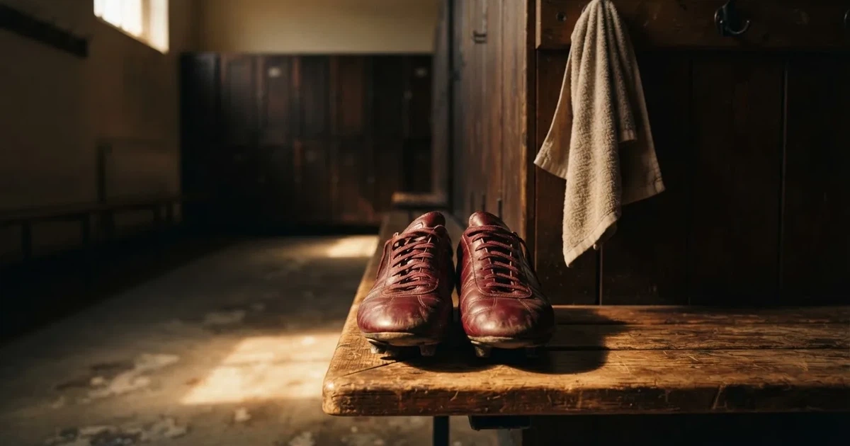 Ein Paar Fussballschuhe steht auf einer Holzbank in einer leeren Umkleide, über der Bank hängt ein Handtuch.