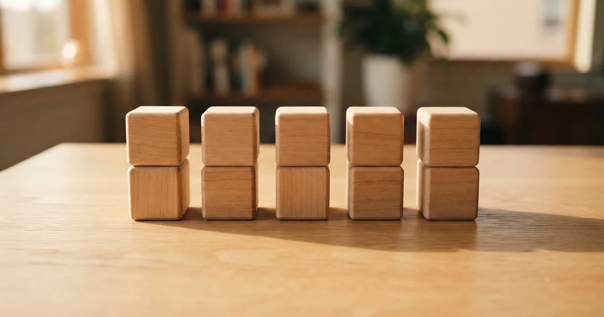 Zehn kleine Holzwürfel liegen in zwei ordentlichen Reihen auf einem hellen Tisch.