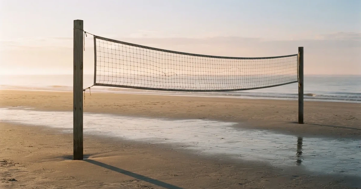 Ein Volleyballnetz spannt sich an einem leeren Sandstrand, das Meer liegt im Dunst.